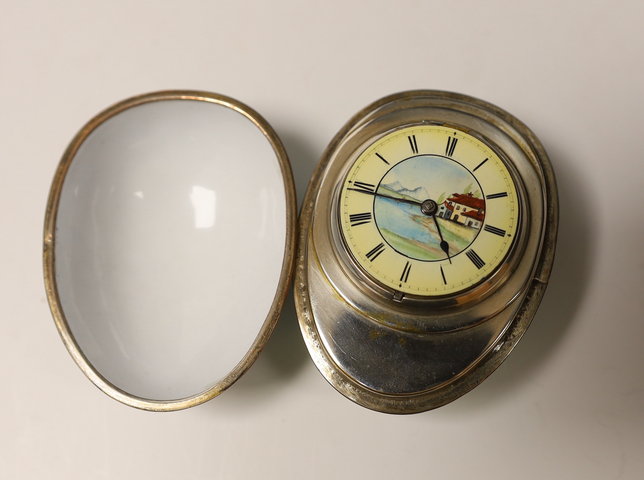 A silver plated and painted enamel egg shaped box and cover, opening to reveal a hinged pocket watch movement by Newsome & Co of London & Coventry, with painted dial, box 73mm.